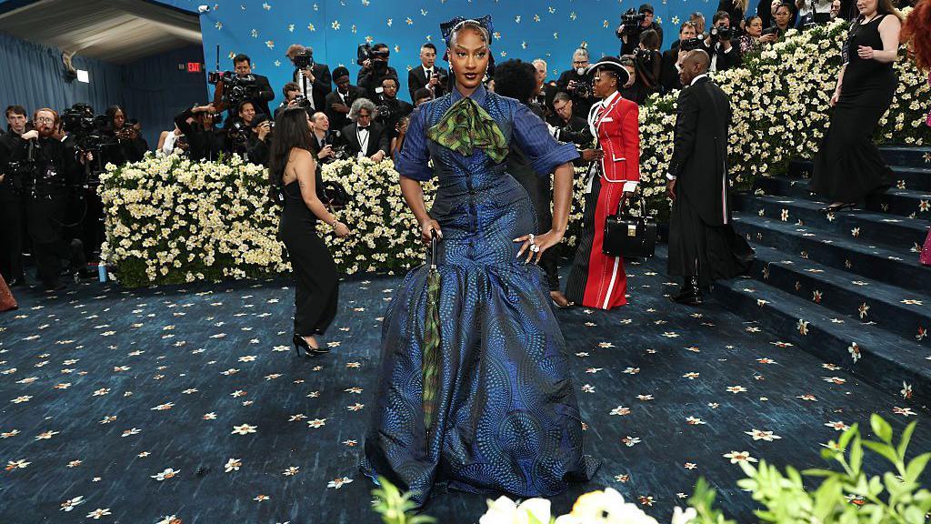 Tems poses at the Met Gala, wearing a blue and green patterned dress