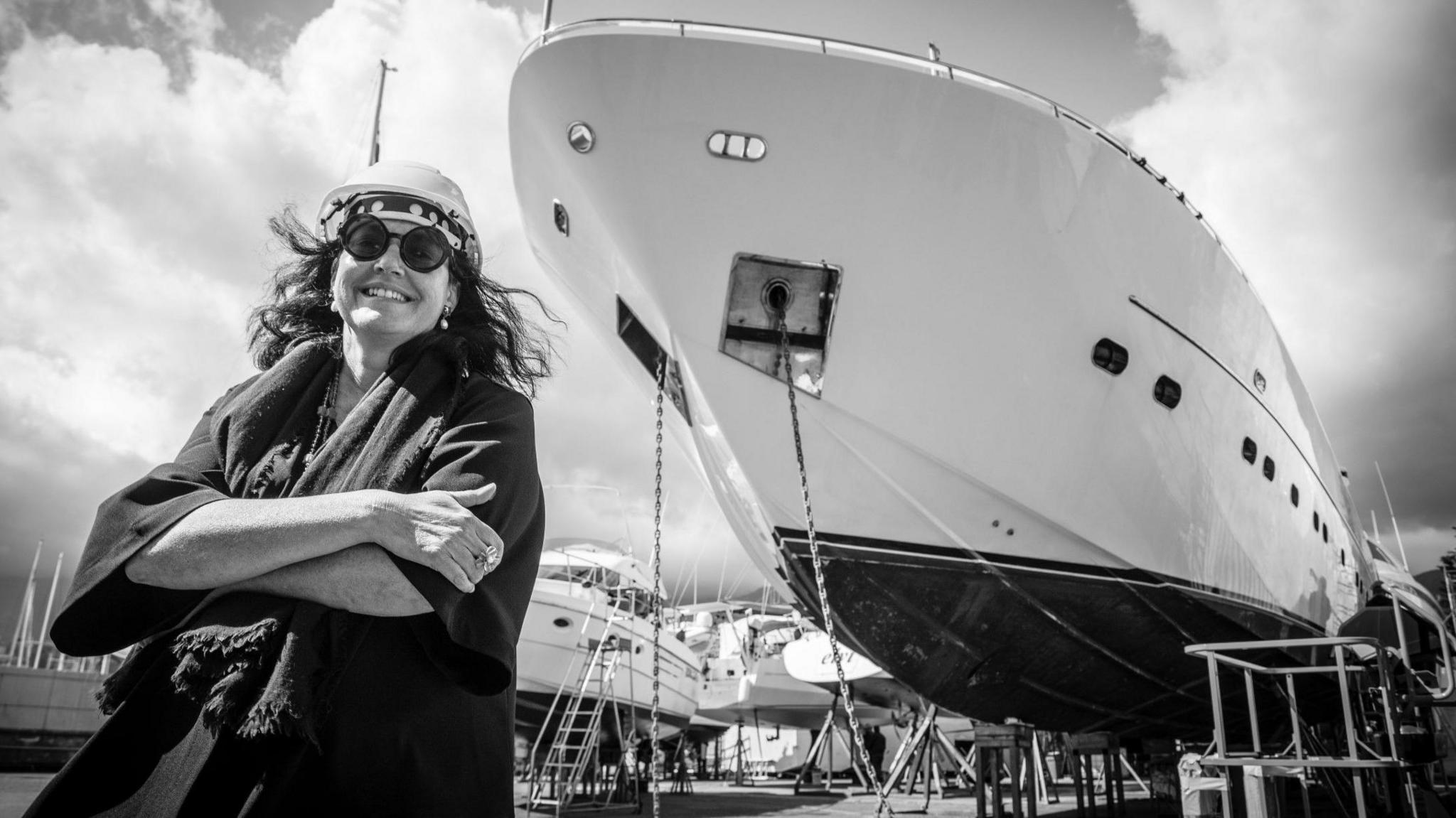 Italian shipbuilder Barbara Armerio smiles at the camera while crossing her arms, in front of a superyacht being built