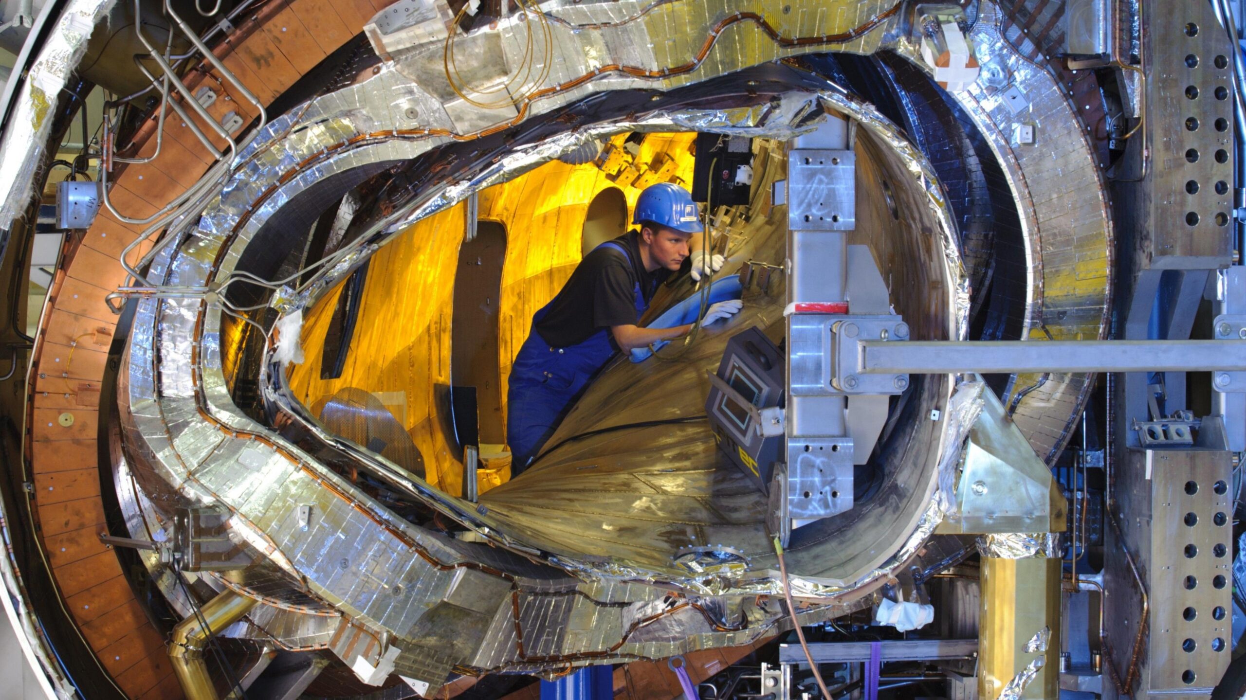 A worker inside the W7-X stellarator, which looks like a twisted and crinkled metal tube.